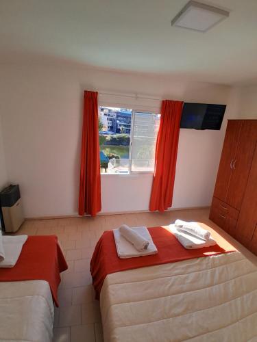 a room with two beds and a window with red curtains at CRISTAL BuenaVista in Villa Carlos Paz