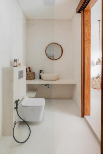 a white bathroom with a toilet and a mirror at Enso Villa and Hotel in Munggu