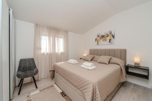 a white bedroom with a bed and a chair at Nelly Apartments in Privlaka