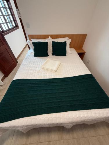 a large bed with green and white sheets and pillows at Casa da Dinda 105 in Rio das Ostras