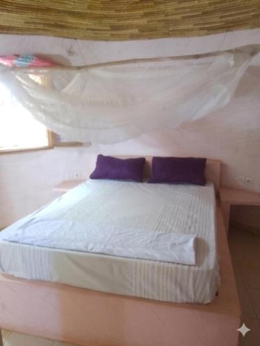 a bedroom with a white bed with purple pillows at Ecolodge EcoFarm Fimela in Fimela