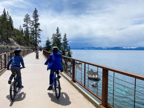 two people riding bikes on a bridge by the water at Lakeland Village #476 in South Lake Tahoe