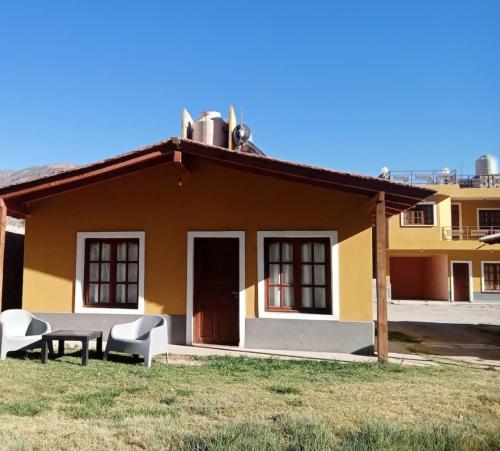 a small yellow house with two chairs and a table at La Posta de Gherard in Maimará
