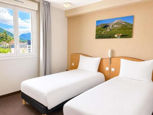 two beds in a room with a window at Hotel Saint Georges Lourdes in Lourdes