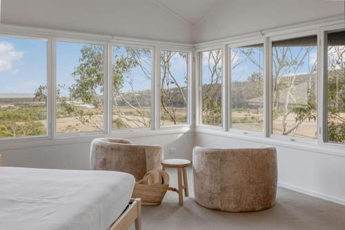 a bedroom with two chairs and a bed with windows at The Ridge House Panoramic views in Aireys Inlet