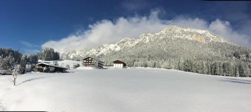 a snow covered field with a house and a mountain at Berghof Haselsberger in Sankt Johann in Tirol