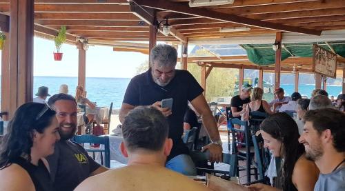 a man looking at his cell phone in a group of people at Paralia Hotel & Taverna in Agia Roumeli