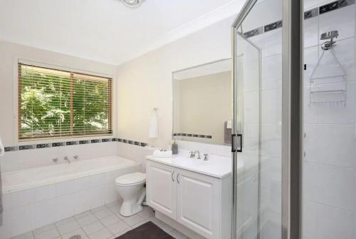 a white bathroom with a tub and a toilet and a sink at Kalamunda Estate with Pool, Fire Pit & BBQ Deck in Bundanoon