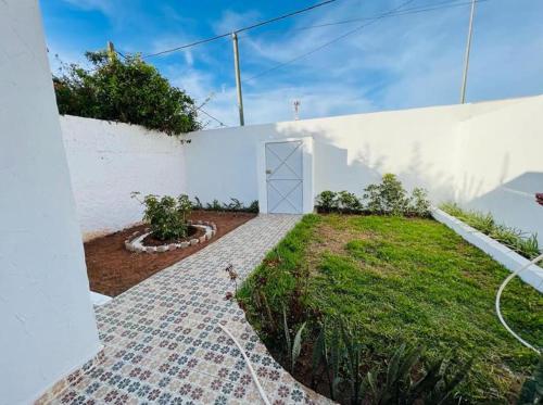 a garden with a white wall and a door at Petit villa centre harhoura Près de la plage in Temara