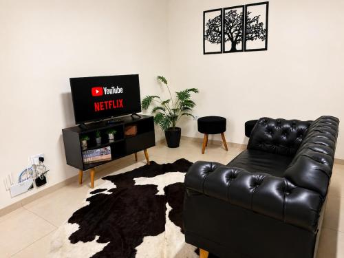 a living room with a black leather couch and a television at Flat 2 quartos em residencial | Ar e garagem in Ourinhos