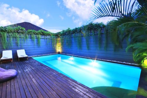 a swimming pool on a wooden deck with two chairs at Letos Kubu 1 in Kuta