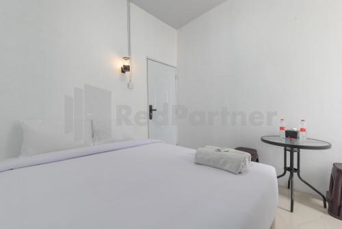 a white bedroom with a bed and a table at Adam Guesthouse Mitra RedDoorz in Bogor