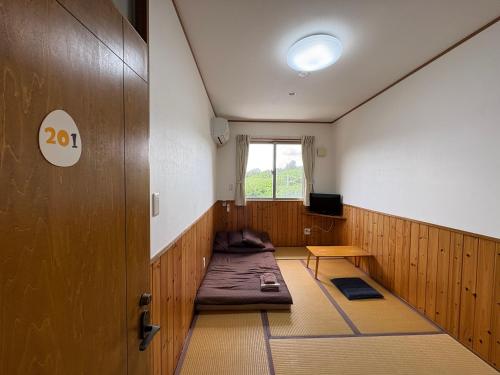 a room with a bed and a door and a window at Hostel Mosura no Tamago in Motobu