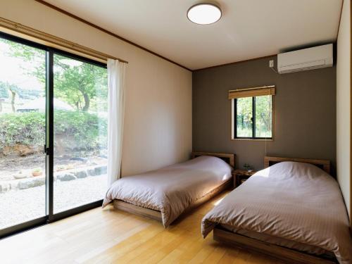 a bedroom with two beds and a large window at Holiday Home 郷 in Minami Aso