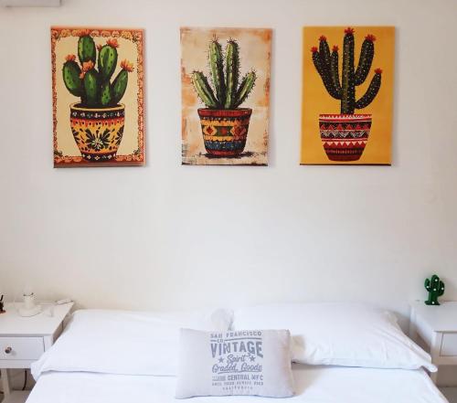 four cactus paintings on a wall above a bed at GuestHouse Gentile Caruso in Torrenova