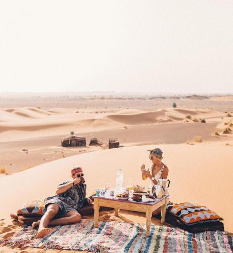 dos personas sentadas en una mesa en el desierto en The Desert Palace, en Merzouga