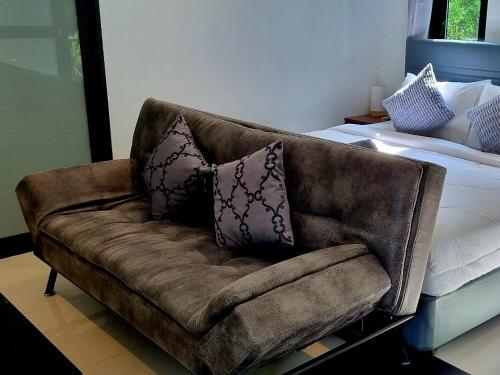 a brown couch sitting next to a bed with pillows at Nua Tone Riverside in Thalang