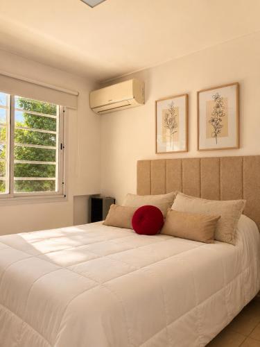 a bedroom with a large white bed with a red pillow at Cabañas Aires del Sur, con gran parque y pileta in Chascomús