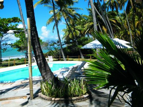 a pool with chairs and palm trees and the ocean at Igarakuê Flat in Japaratinga