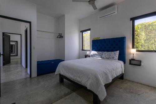a bedroom with a bed with a blue headboard and two windows at Las Palmas Hotel - Cerritos Beach in El Pescadero