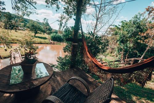 a hammock with a table and chairs and a river at Chalé dos Alves in Morro Azul