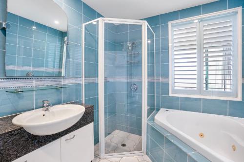 a blue tiled bathroom with a sink and a tub at Alexandra on the Pacific in Mooloolaba