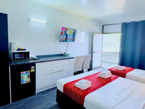 a room with two beds and a kitchen with a microwave at Tropical Gateway Motor Inn in Rockhampton