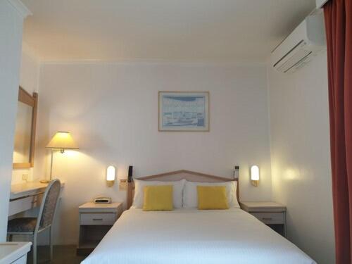 a bedroom with a white bed with two yellow pillows at Arden Motel in Melbourne