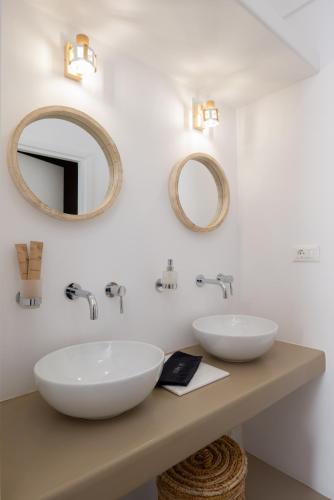 two sinks on a counter in a bathroom with mirrors at Lithos Suites Sifnos in Kamares