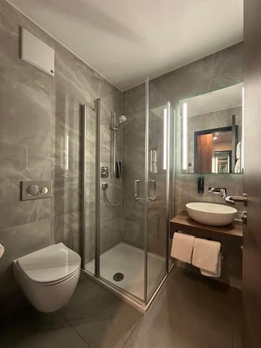 a bathroom with a shower and a toilet and a sink at Intergroup Business & Design Hotel Ingolstadt in Kösching