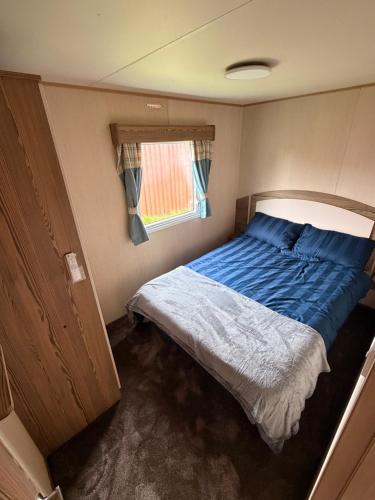a bedroom with a bed with a blue comforter and a window at Elite Retreat Caravan in Blackpool