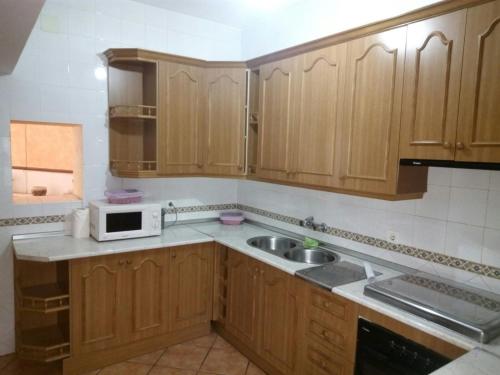 cocina con armarios de madera, fregadero y microondas en Casa Rural Pastora Marcela, en Saceruela