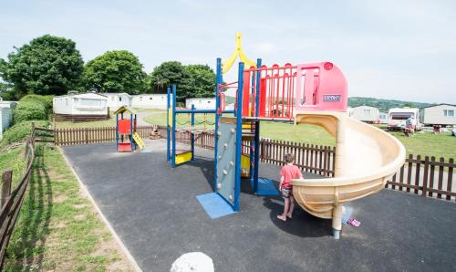 a boy is standing next to a playground at Sandaway Holiday Park in Combe Martin
