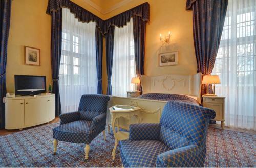 a bedroom with a bed and two chairs and a television at Château Liblice in Byšice