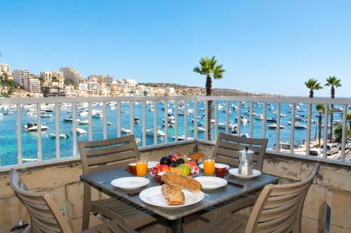 a table with food on a balcony with a view of a harbor at Blue Harbour 2 bedroom Seafront Apartments with large terrace with spectacular sea views - by Getawaysmalta in St. Paul's Bay