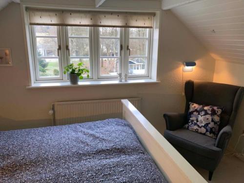 a bedroom with a bed and a chair and a window at Private country side apartment in Holstebro