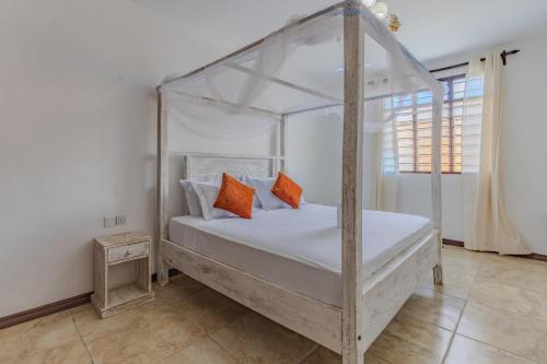 a bedroom with a white canopy bed with orange pillows at Solana Pearl Beach Private Villa in Tiwi