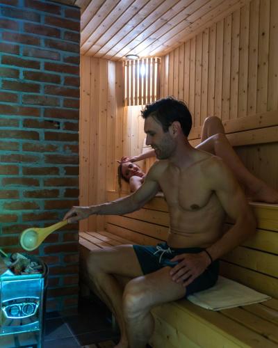 a man sitting in a sauna holding a brush at Lisine Lepo Mesto Guesthouse & Spa in Strmosten