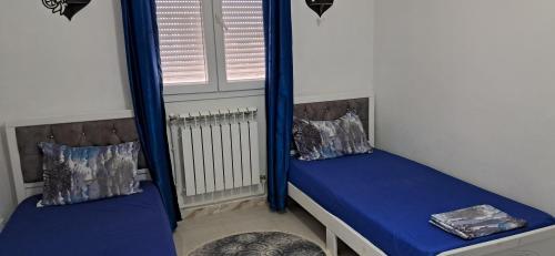 a room with two beds with blue curtains and a window at Appartement meublé in Constantine