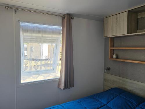 a bedroom with a window and a blue bed at Sous les Pins dans camping 4 étoiles MH familial 322 6 à 8 couchages 2 salles de bain 2 WC in Saint-Julien-en-Born