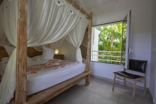 a bedroom with a canopy bed with a chair and a window at Majesty Palm Hôtel in Saint-François