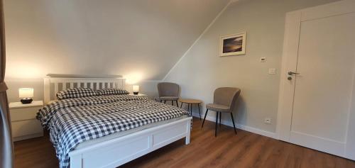 a white bedroom with a bed and two chairs at Dom nad Szelmentem in Przejma Wysoka