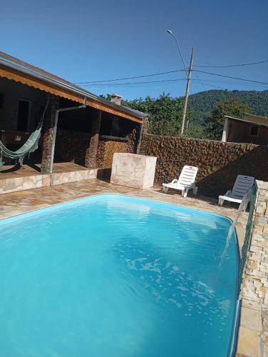 a large swimming pool with two chairs and a house at Chácara sonho meu in Jacutinga
