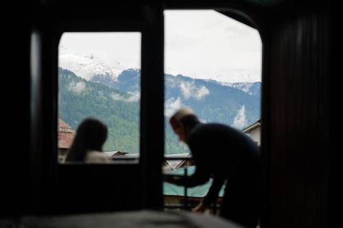 a man and a woman sitting at a table looking out the window at Kanishka, Manali - AM Hotel Kollection in Manāli