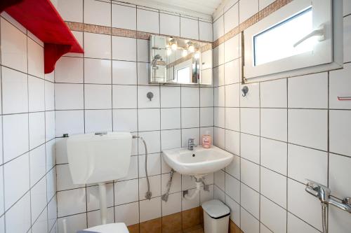 ein weiß gefliestes Badezimmer mit Waschbecken und Toilette in der Unterkunft Elgrecosuits in Limenaria