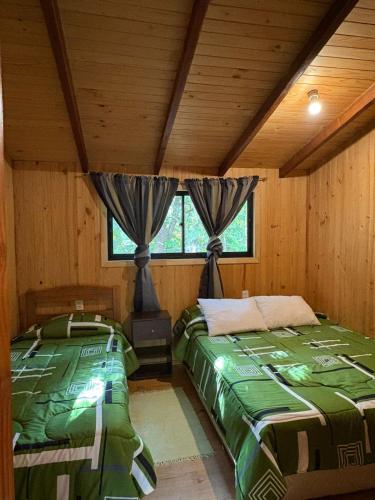two beds in a room with wooden walls at Parcela Peumayen casa 1 in Coñaripe