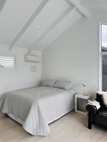 a white bedroom with a bed and a chair at Luxury Poolside Studio Near Hobbiton in Matamata