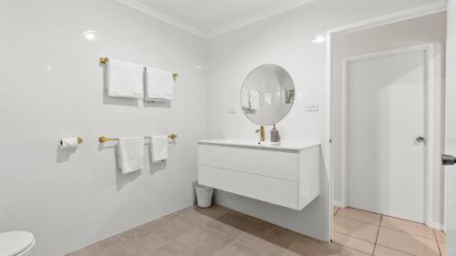 a white bathroom with a sink and a mirror at Honeybee House Cottage in the Rainforest in Kuranda