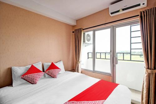 a bedroom with a bed with red pillows and a window at Hotel O Tridasa in Medan