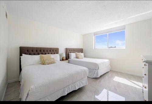 two beds in a white room with a window at Ocean Reserve Miami Sunny Isles Collins Ave in Sunny Isles Beach